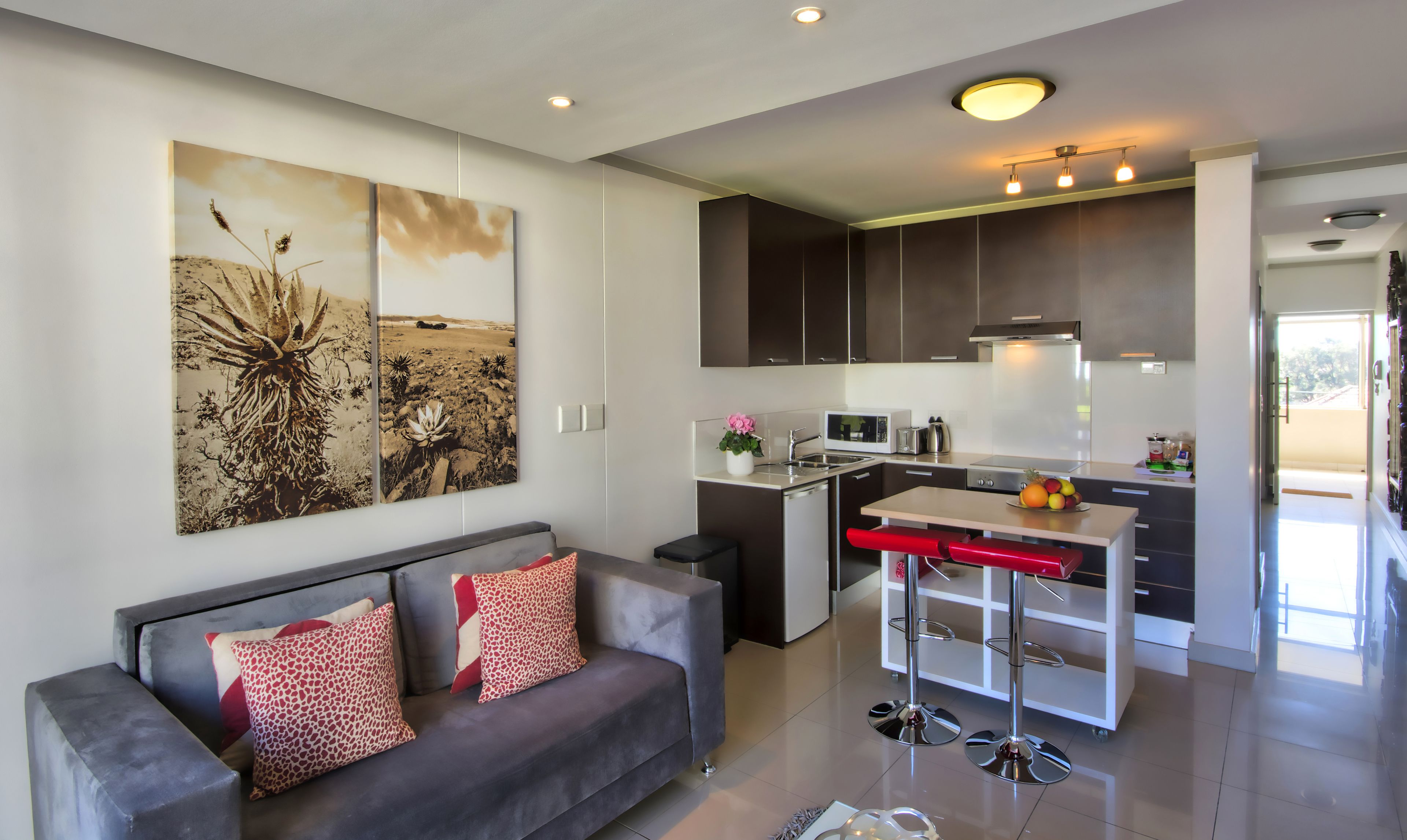 A modern kitchen with dark cabinets, a microwave, and a sink. There is a dining area with a table and chairs.