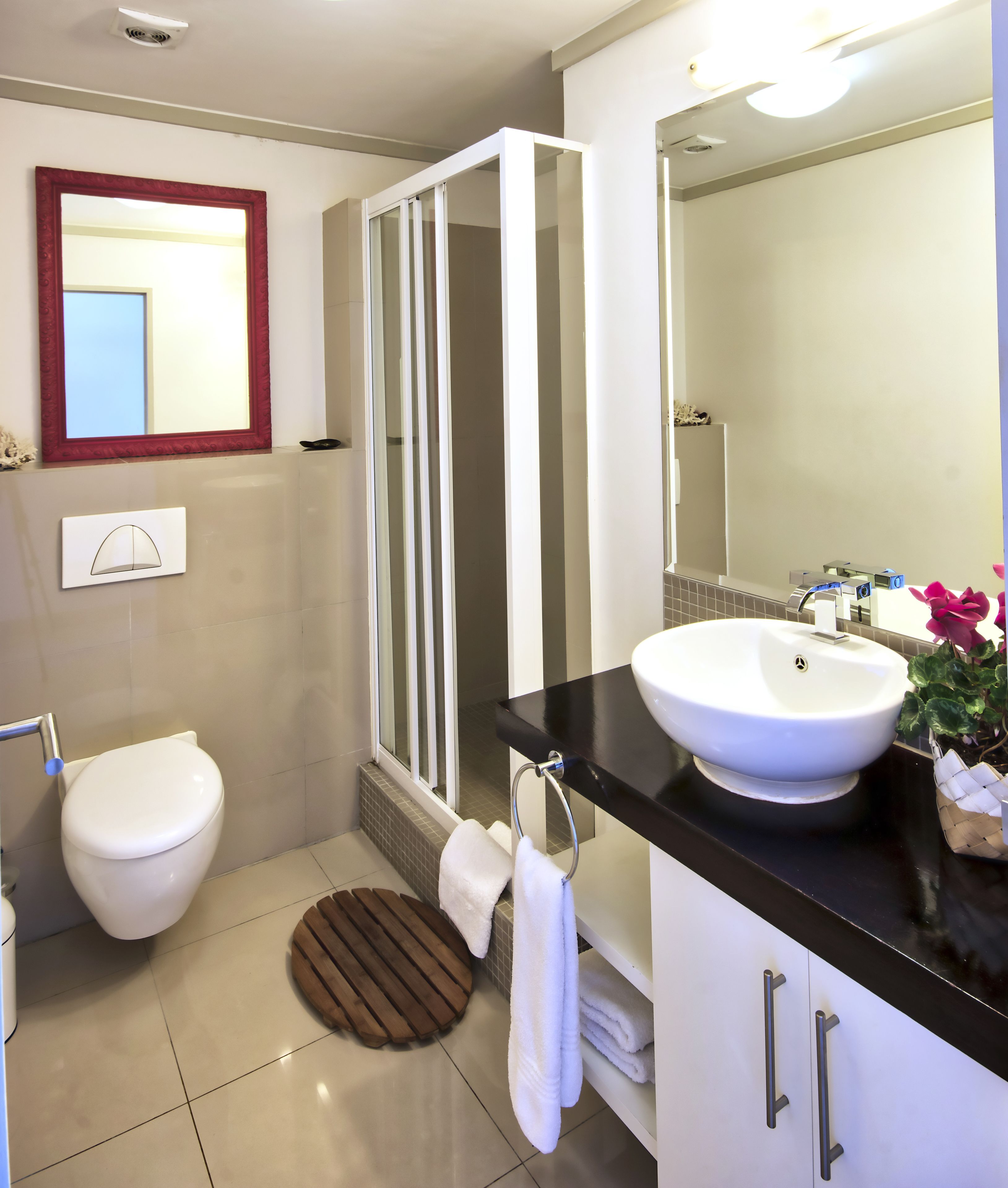 A modern bathroom with a white toilet, a glass shower enclosure, a sink with a black countertop, and a mirror above the sink.