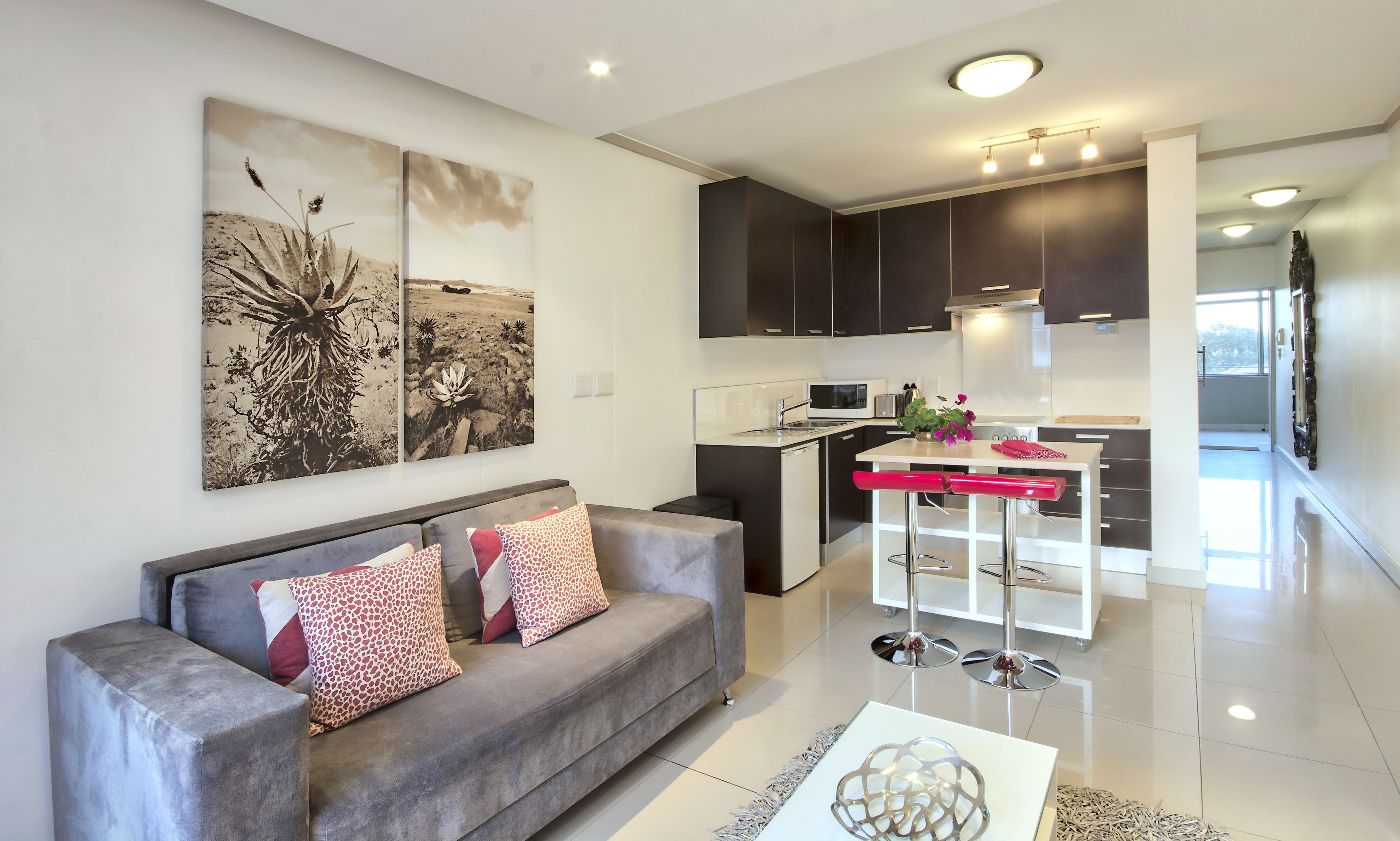 A modern living room with a grey sofa, a coffee table, and a kitchen area with a white countertop, black cabinets, and a microwave.