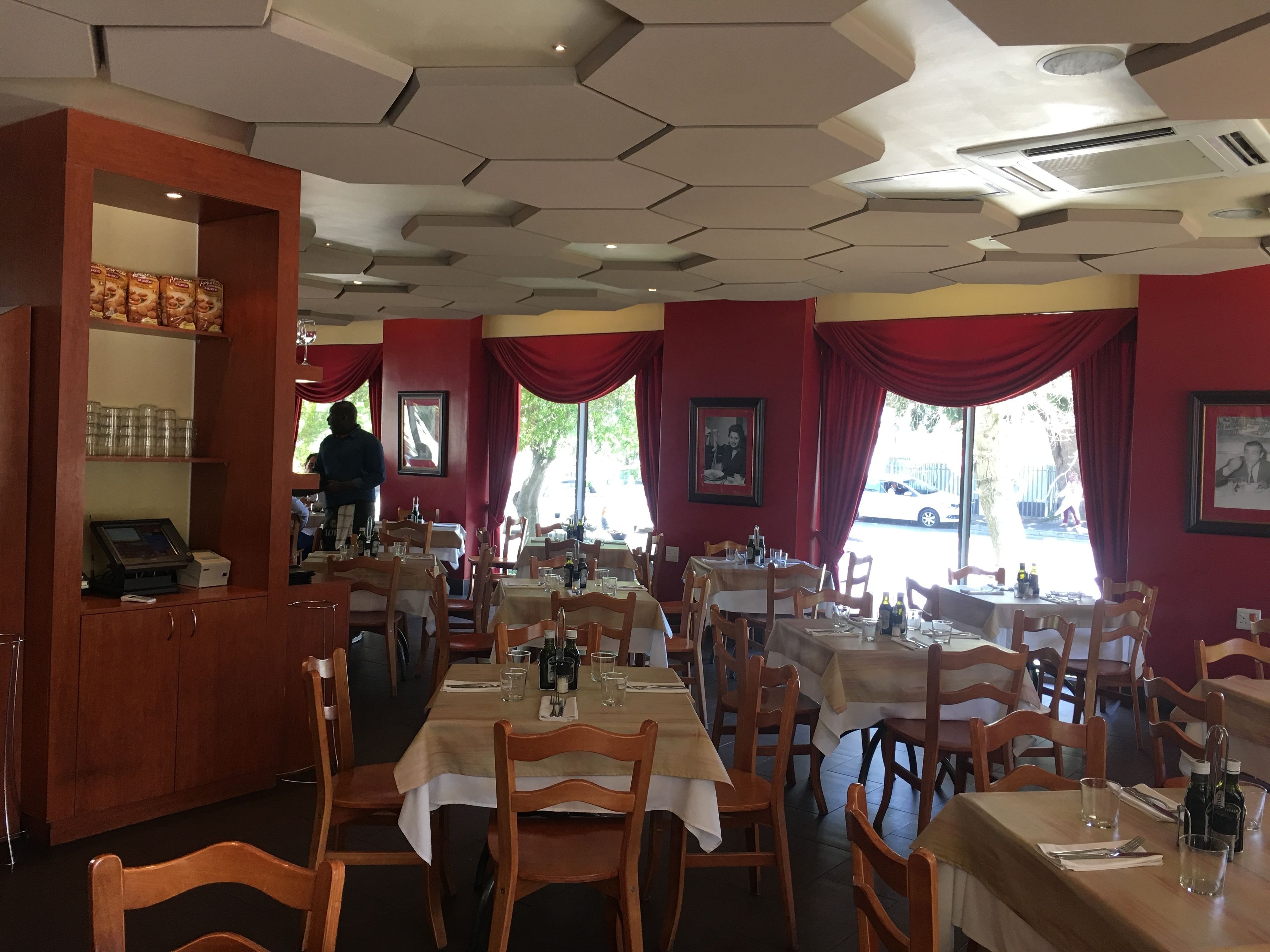 Ein Restaurantinnenraum mit Holztischen, roten Vorhängen und einer Bar.