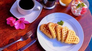 Una mesa de madera con waffles, café, una bebida caliente y un jugo de frutas.