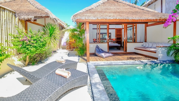 Un resort con bungalós sobre el agua con techo de paja, piscina y zonas de estar al aire libre.