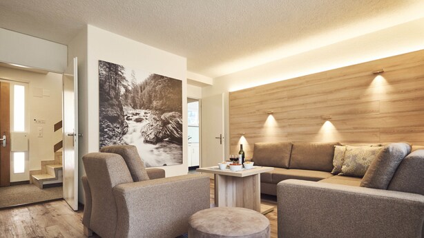 A modern living room with a wooden accent wall, a sofa set, a coffee table, and a painting of a waterfall. - Private Holiday Homes by SOLARIA (Davos)