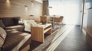 A modern hotel room with a wooden floor, a sofa, a coffee table, and a dining area with chairs and a table. - Private Holiday Homes by SOLARIA (Davos)