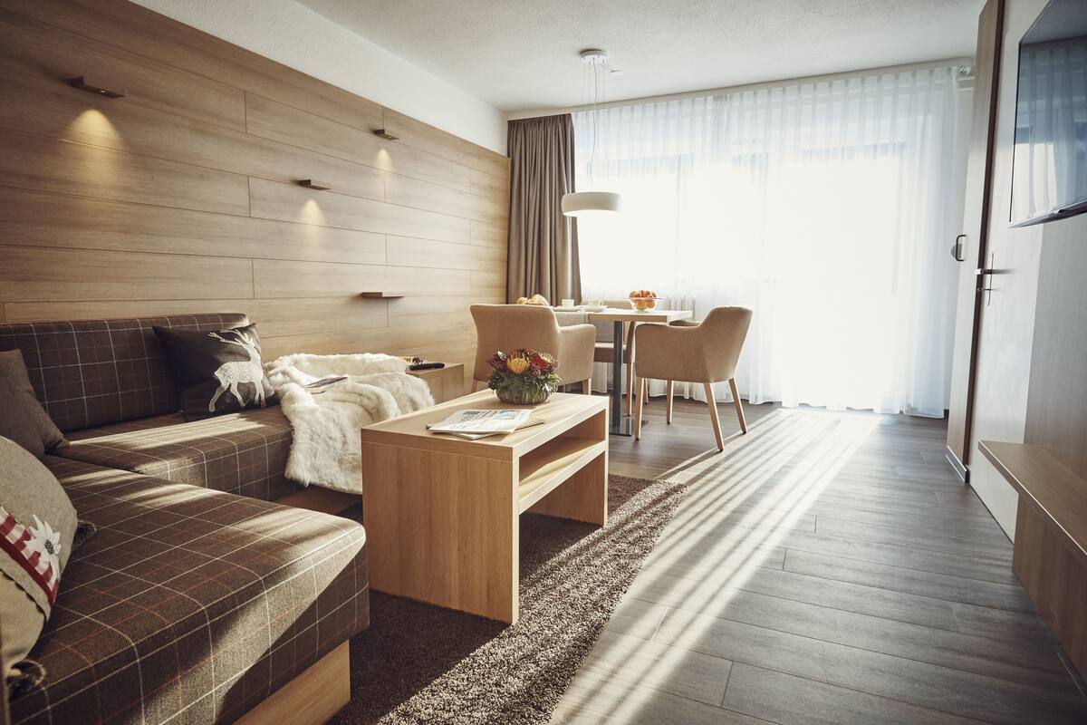 Moderni hotellihuone, jossa on puulattia, sohva, sohvapöytä sekä ruokailutila, jossa on tuoleja ja pöytä.