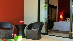 A balcony with wicker chairs, a potted plant, and a view into a room with a bed and a lamp. - Baan Lompai (Krabi)