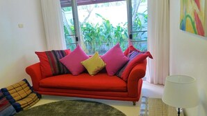 A red sofa with colorful cushions, a green rug, and a lamp. - Baan Lompai (Krabi)