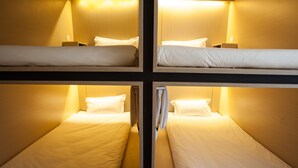 A four-bed dormitory room with bunk beds, each with a pillow and a small bedside table. - Cubic Bed Pratunam - Hostel (Bangkok)