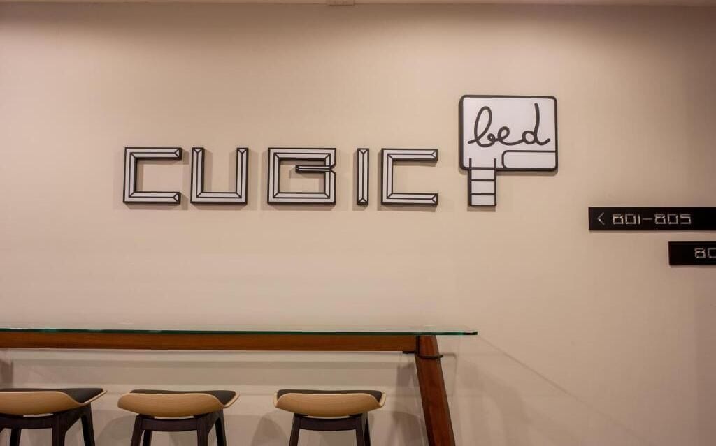 A wall with the word "CUBIC" and a bed icon, a glass table, and three chairs.