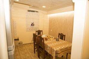 A dining room with a table set for four, wooden chairs, a patterned tablecloth, and a window with curtains. - Your Hostel (Yerevan)