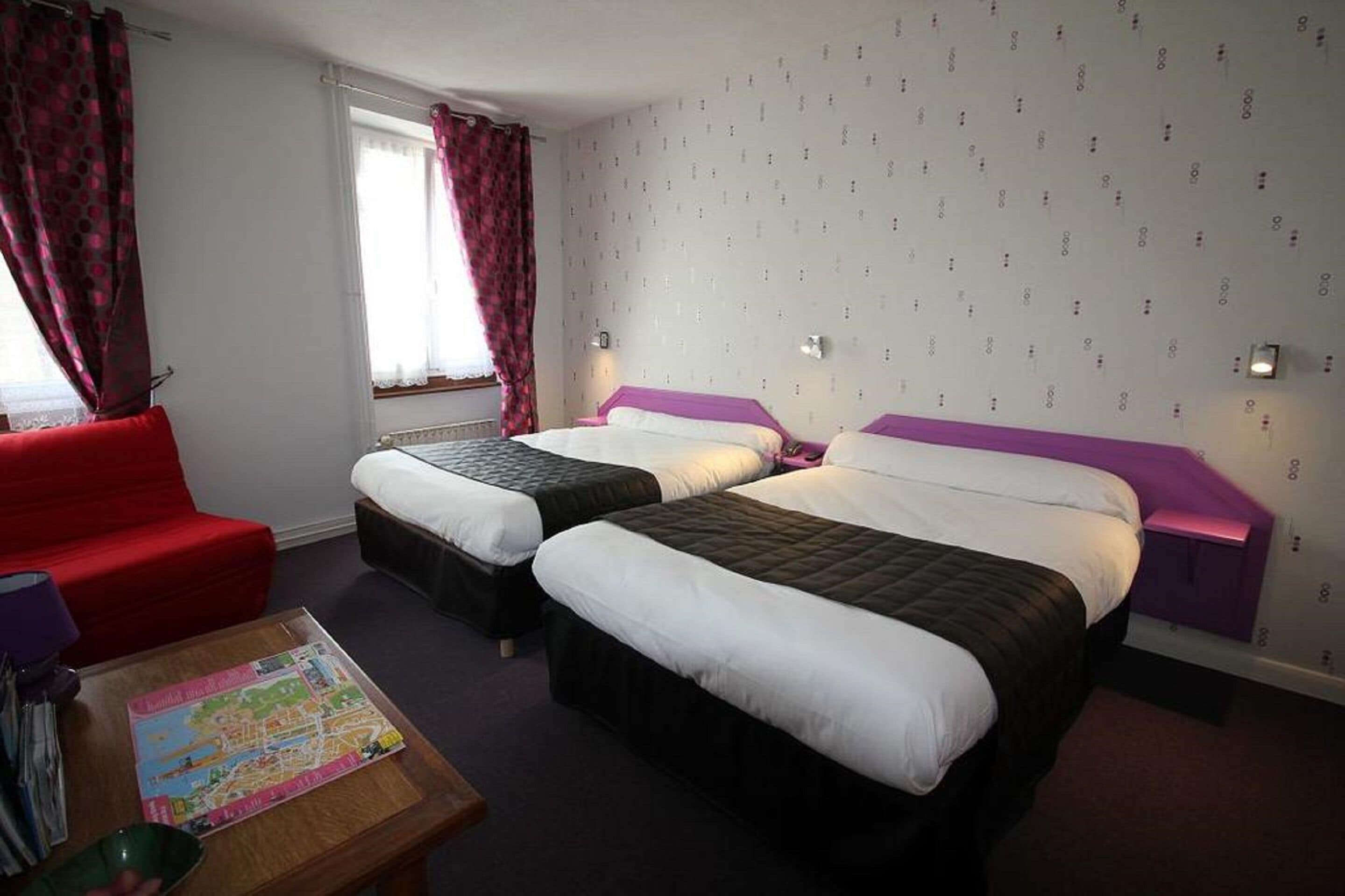 Quarto de hotel com duas camas, um sofá vermelho, uma mesinha com um mapa e papel de parede estampado.