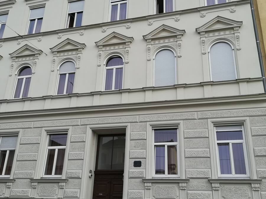 Un edificio de varios pisos con fachada simétrica, ventanas uniformemente espaciadas con persianas, una entrada central y molduras decorativas.