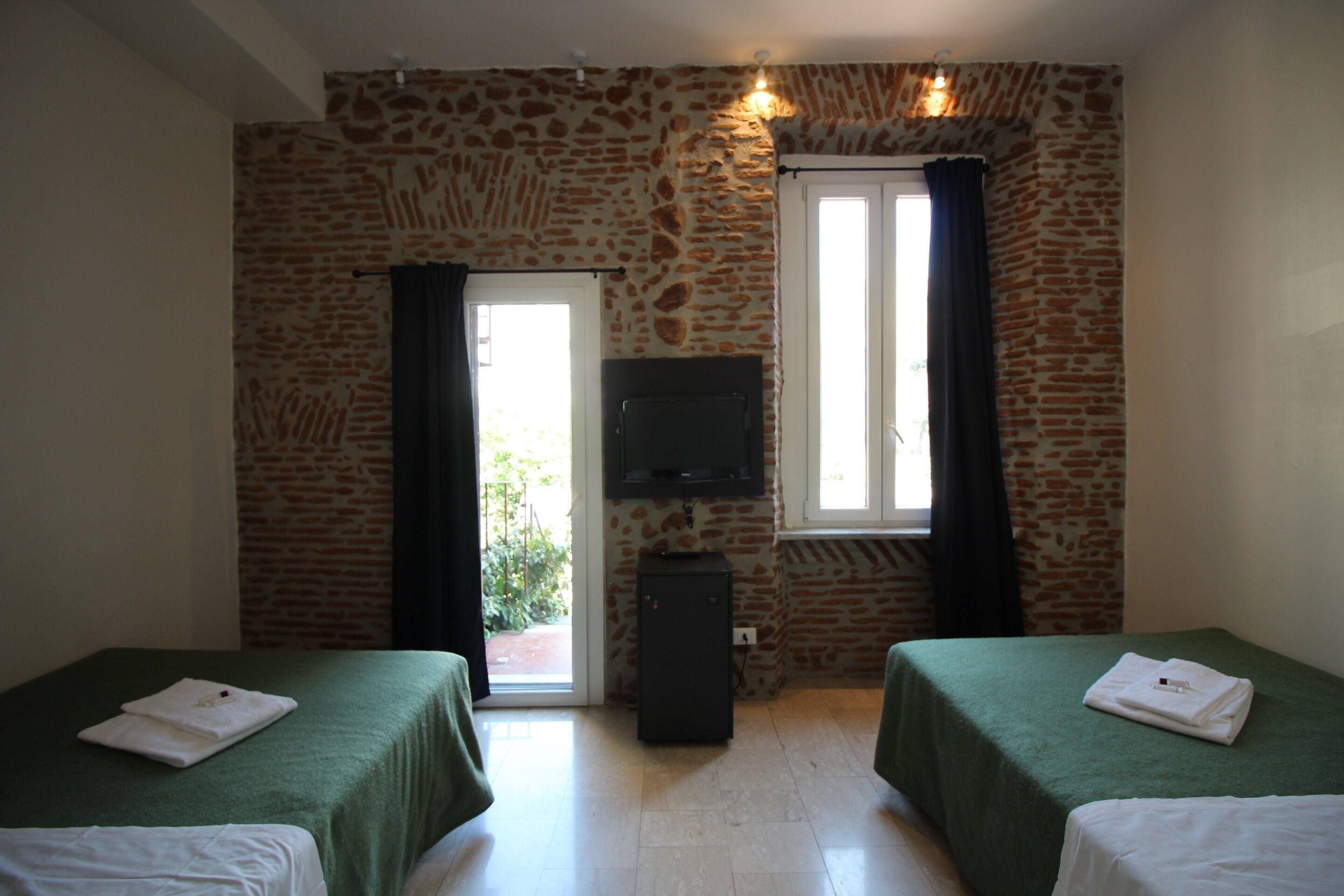 A room with two beds, a television, and a stone wall.
