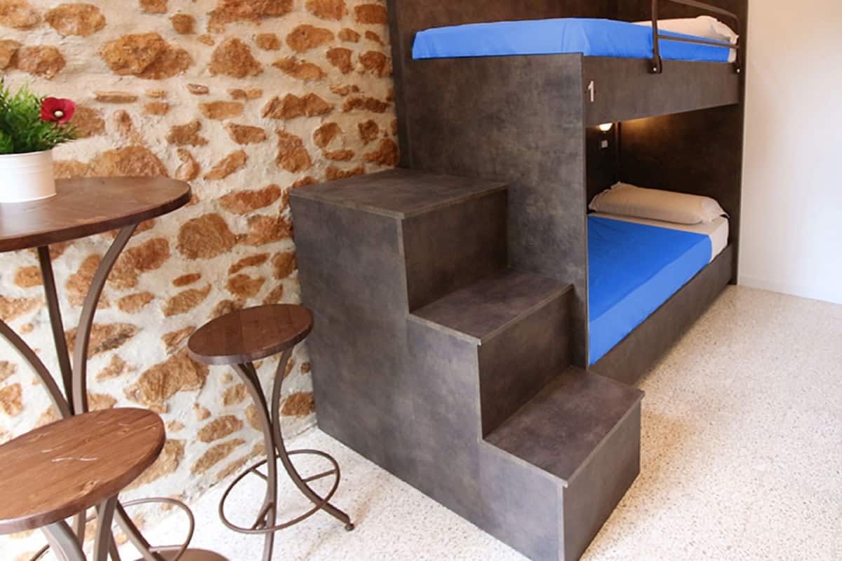 A bunk bed with a blue mattress, a small table with a plant, and a stone-patterned wall.