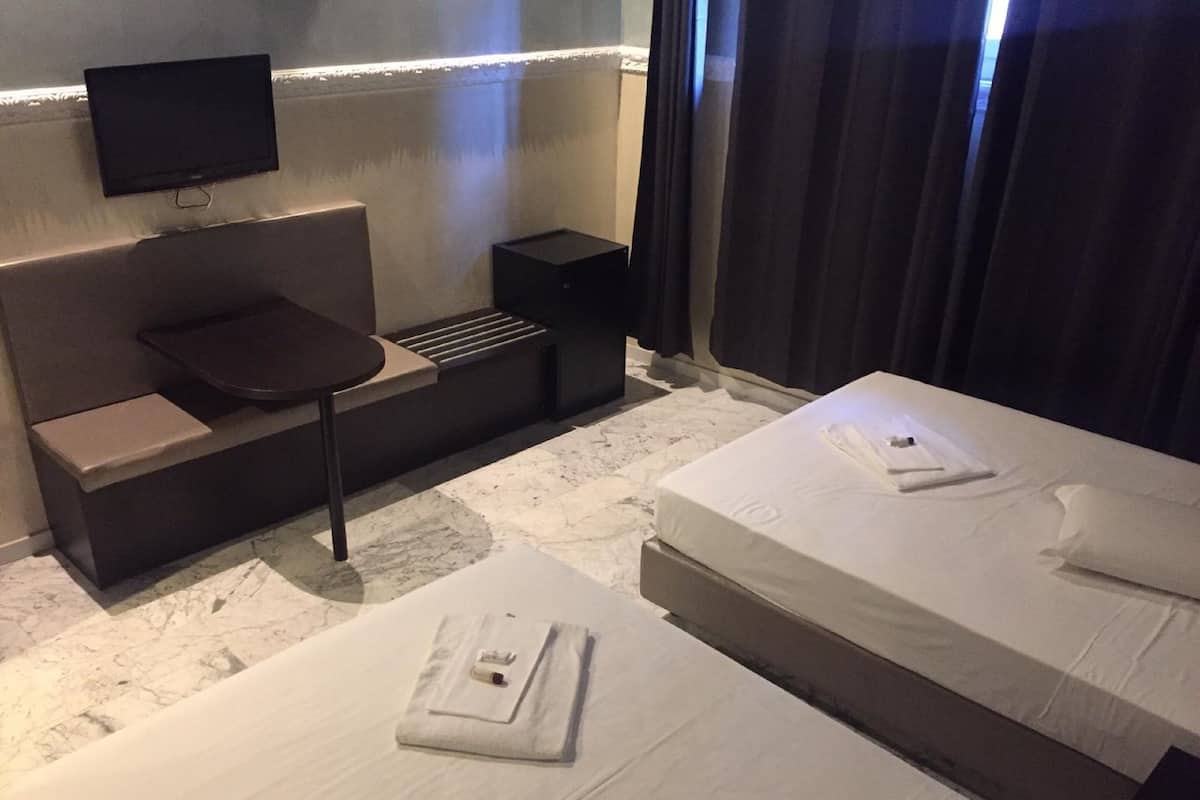 A hotel room with a sofa bed, a single bed, a TV mounted on the wall, and a small table.