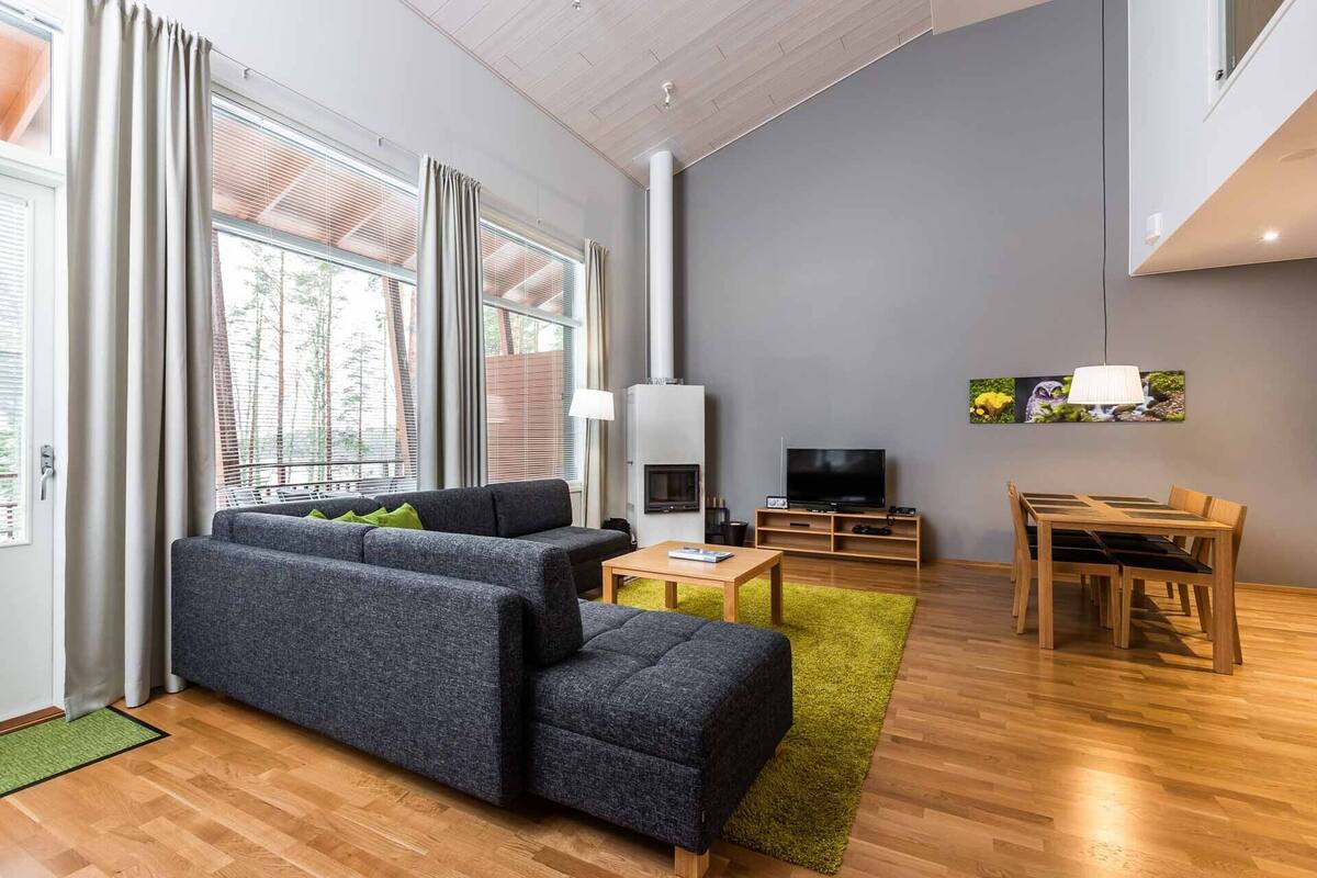 A modern living room with a grey sofa, wooden dining table, and a flat-screen TV.