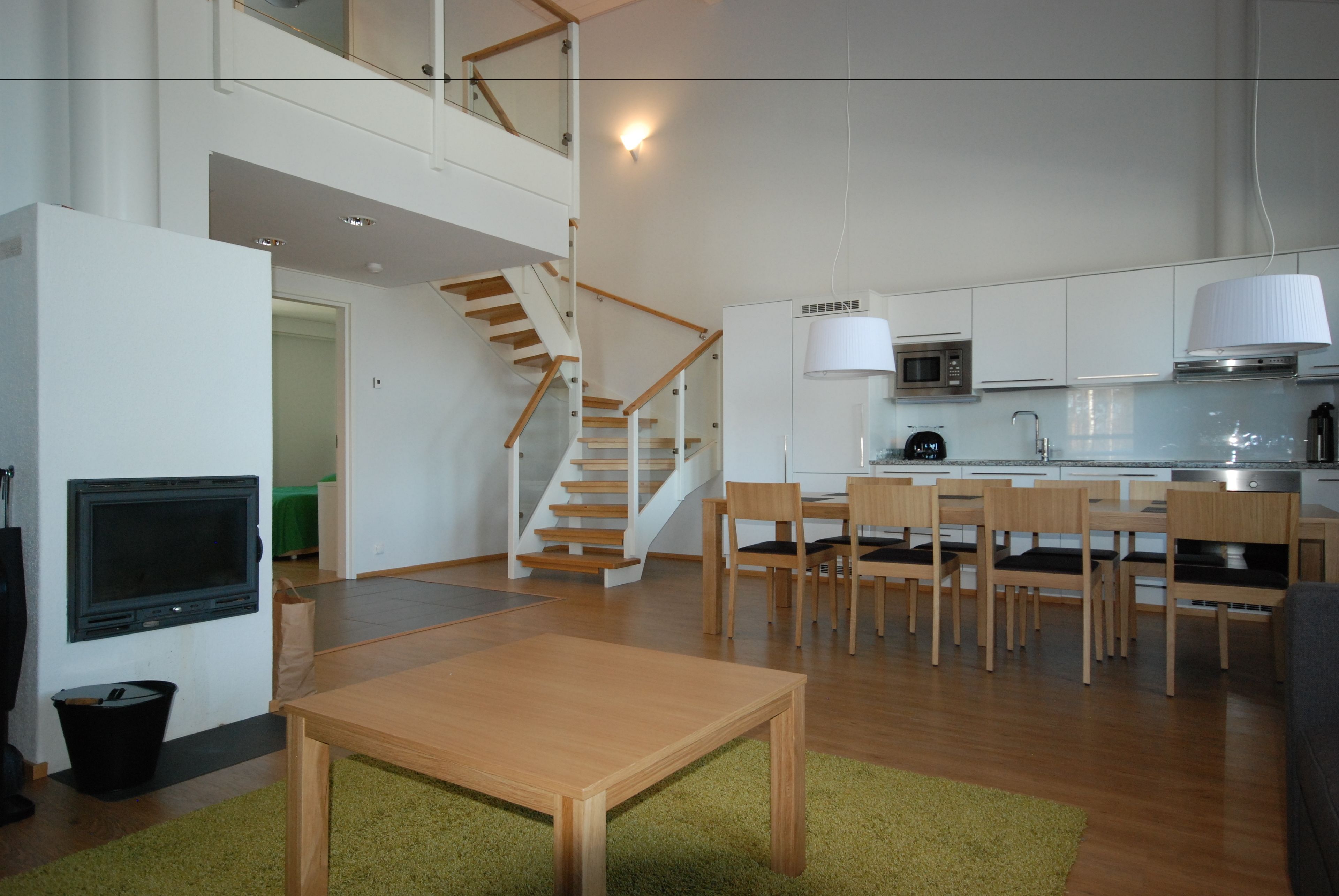 A modern kitchen with white cabinets, a microwave, and a stove. There is a dining area with a wooden table and chairs. A staircase leads to an upper level.