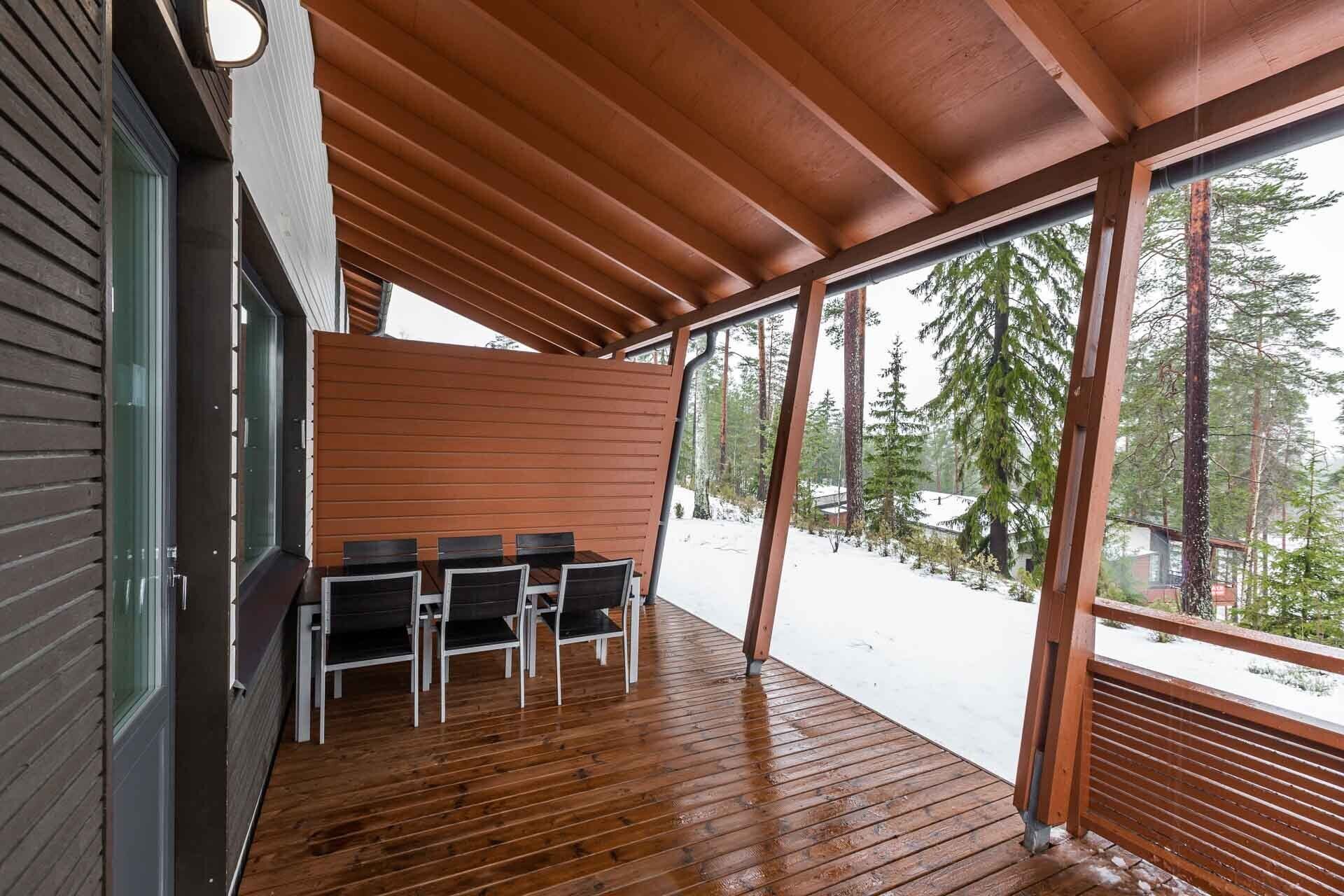 Un espace extérieur abrité, doté d’une terrasse en bois et offrant une vue sur une forêt enneigée.
