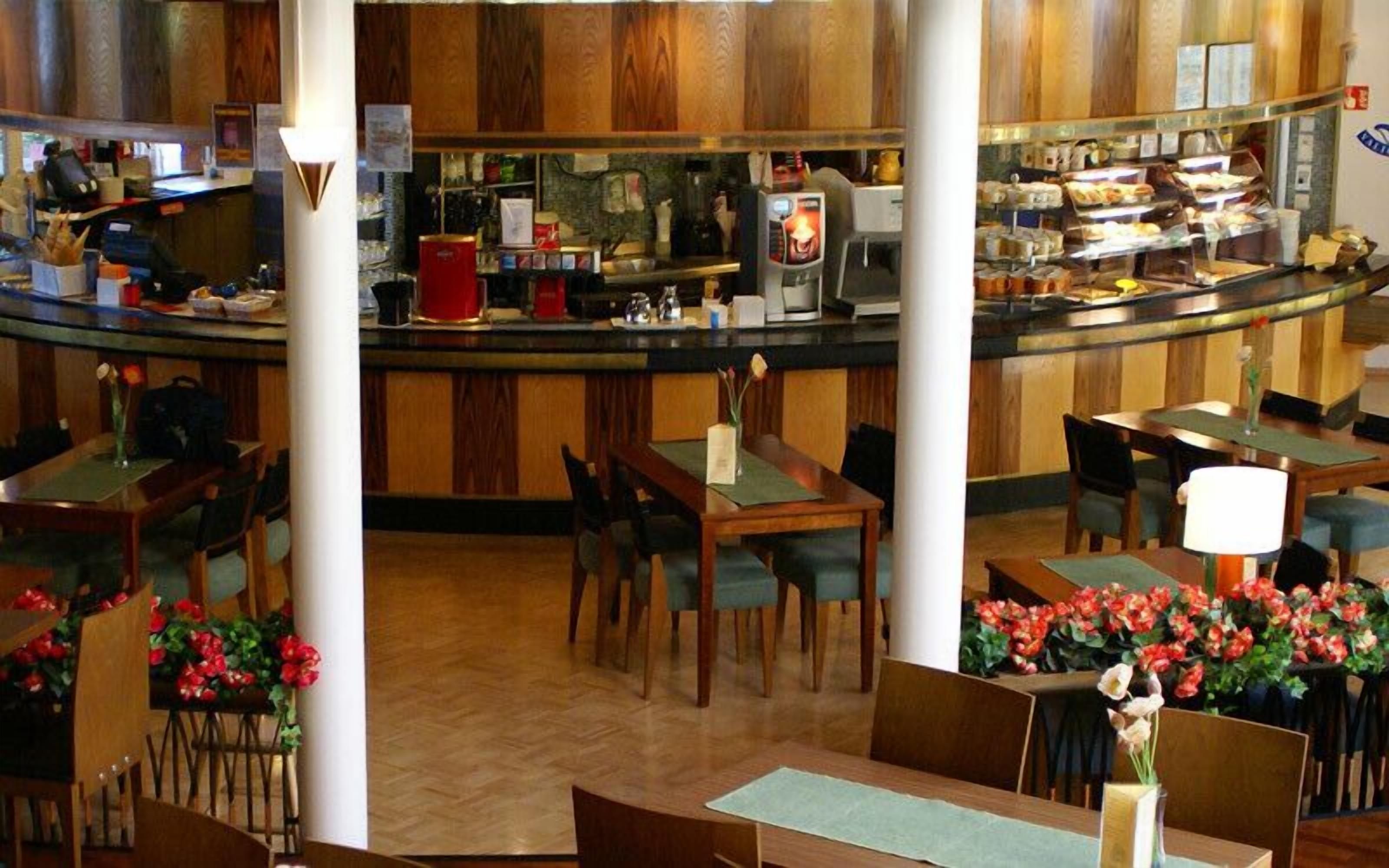 A restaurant with wooden paneling, a counter with a coffee machine, and tables with chairs.