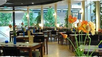 A restaurant with multiple tables and chairs, indoor plants, and a view of trees outside.