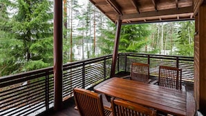A wooden deck with a table and chairs, surrounded by a metal railing, overlooking a forested area. - Imatran Kylpylä Spa Apartments (Imatra)