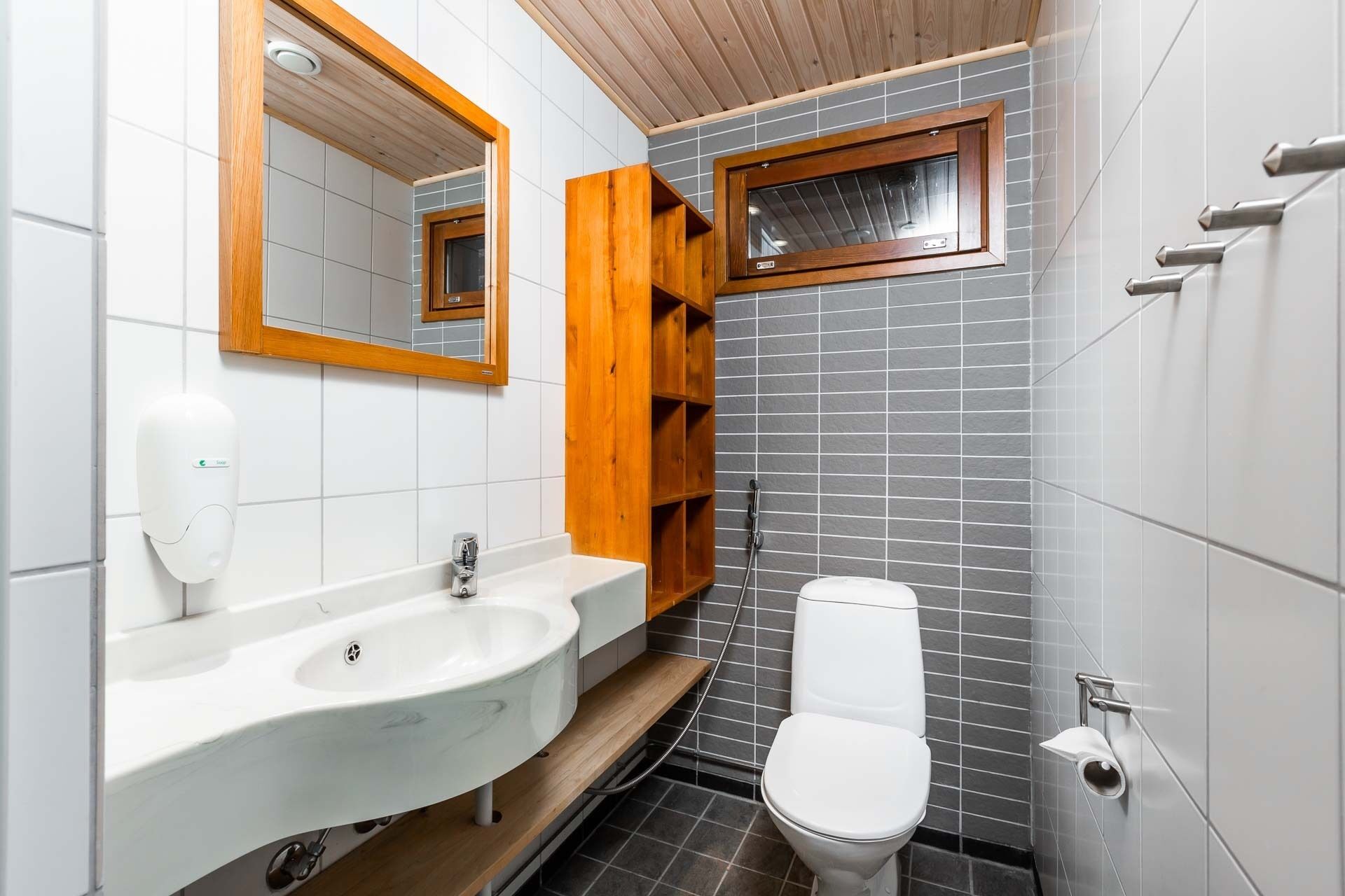 A modern bathroom with a white sink, wooden shelves, a toilet, and a window.