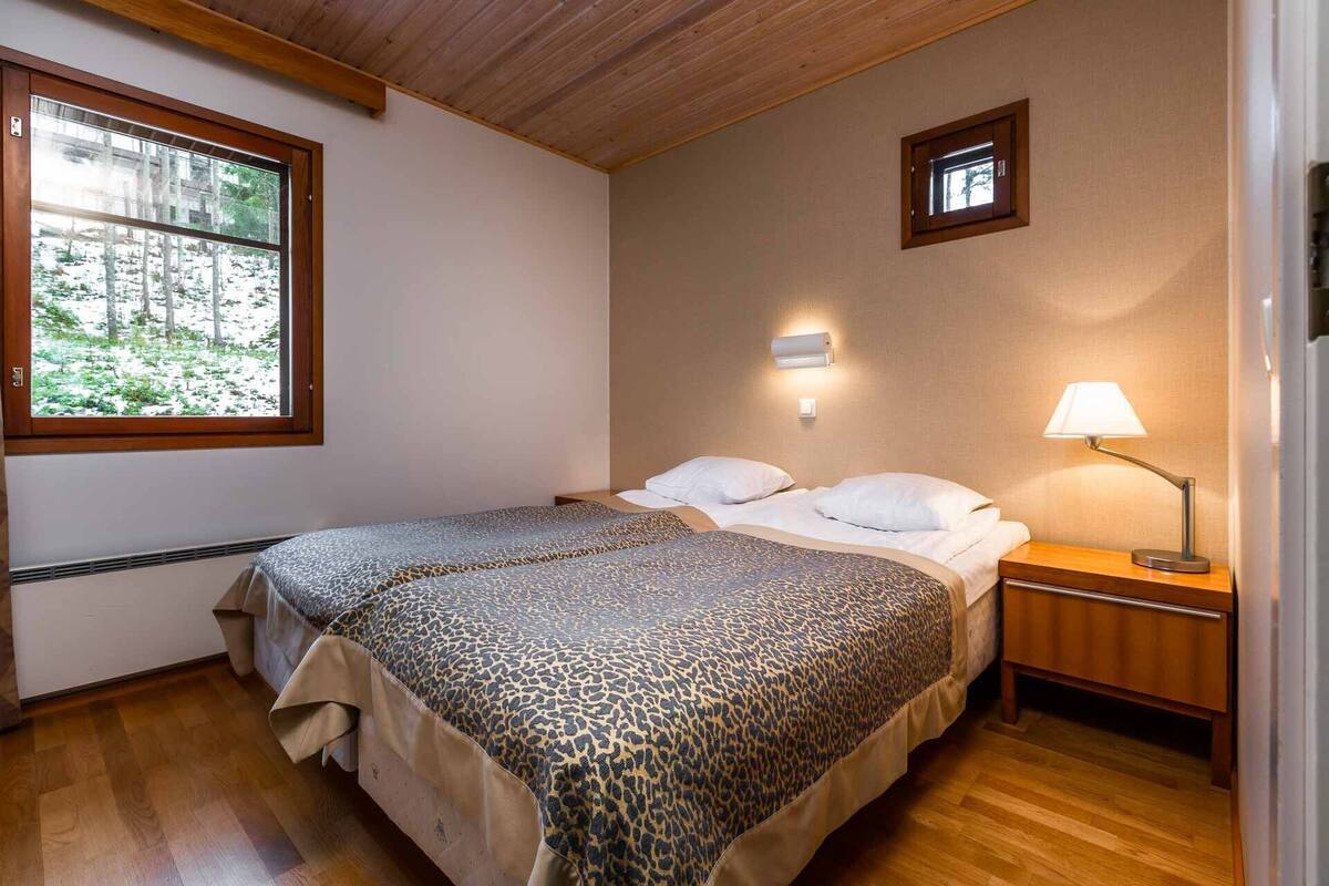 A bedroom with a bed, a nightstand, a lamp, and a window with a view of trees.