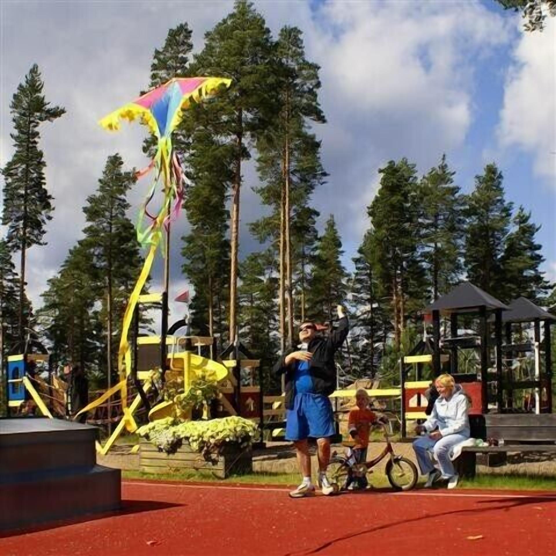 Un parc avec une aire de jeux, des bancs et un grand cerf-volant jaune.