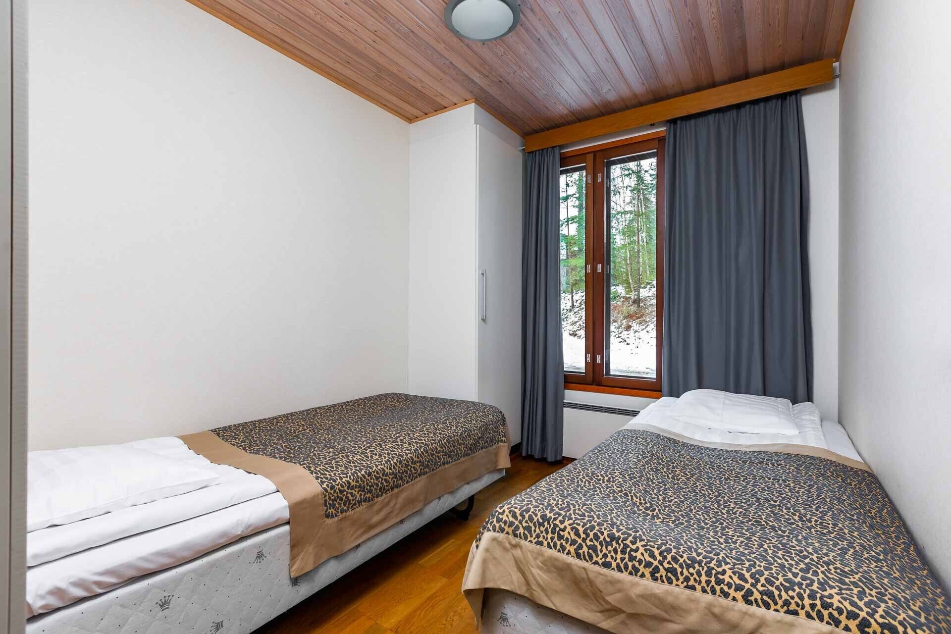 Une chambre avec deux lits, un plancher en bois, une fenêtre avec des rideaux et un luminaire au plafond.