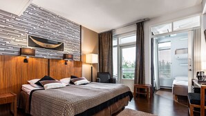 A modern hotel room with a large bed, a wooden headboard, a desk, and a view of the outdoors. - Imatran Kylpylä Spa Apartments (Imatra)