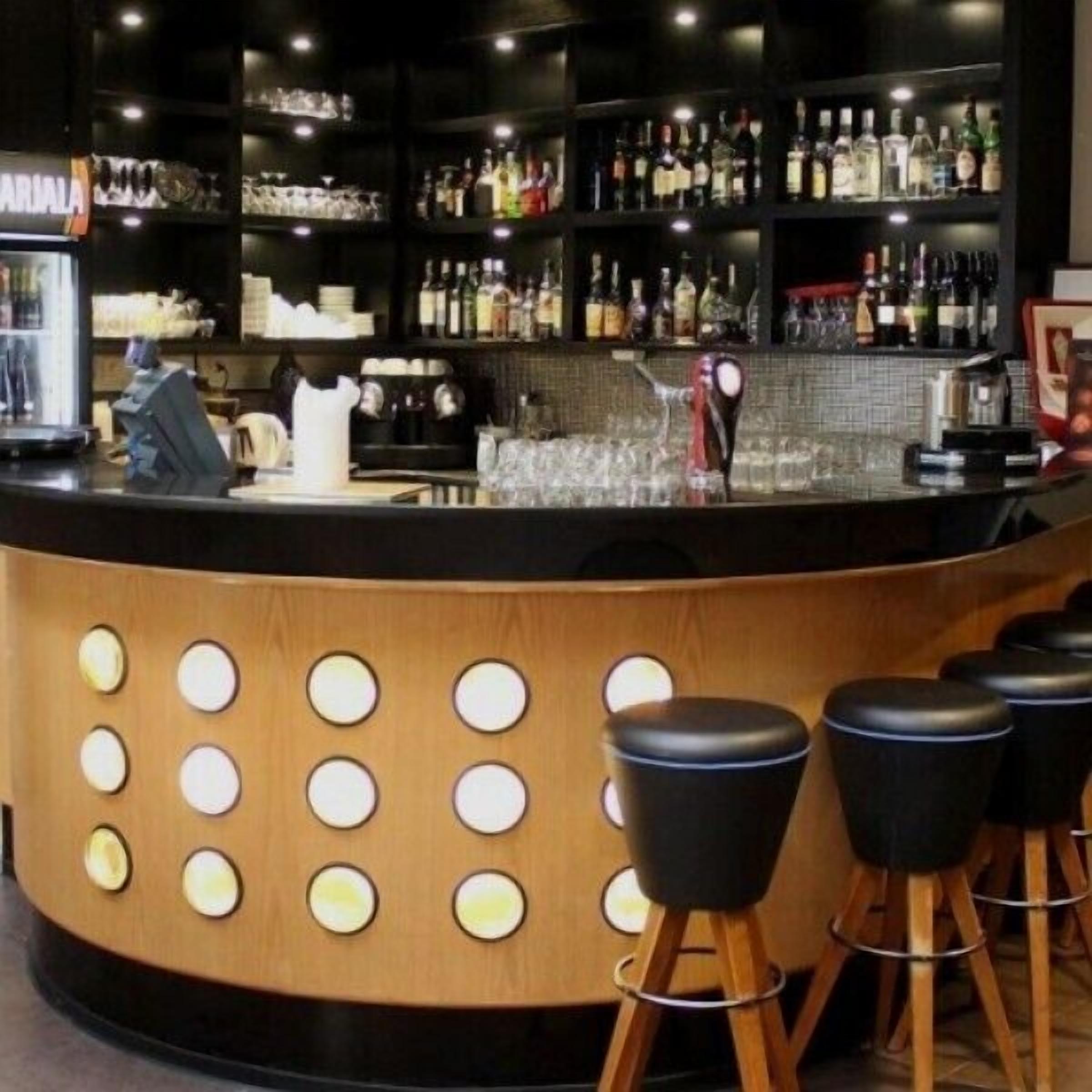 A bar area with a curved counter, multiple stools, and a variety of bottles and glasses on shelves.