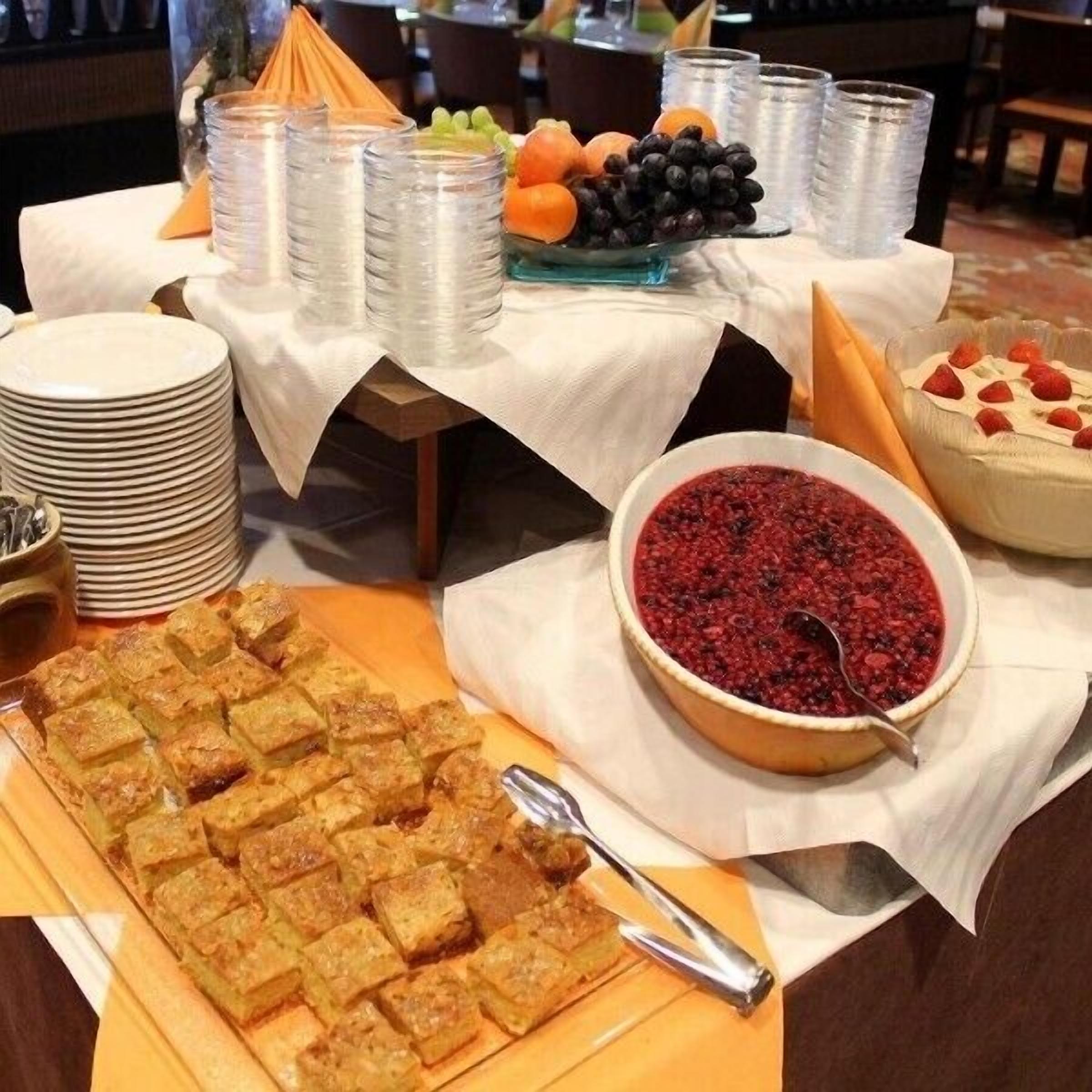 A buffet table with various food items, including a dish of cubes, a bowl of red fruit compote, and a dessert topped with strawberries.