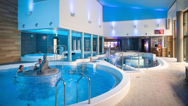 A large indoor swimming pool with multiple sections, including a central area with a dolphin statue and surrounding smaller pools. - Imatra Spa Sport Camp - Hostel (Imatra)