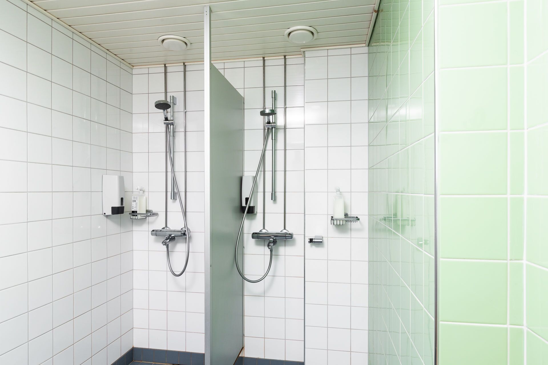 Un baño moderno con paredes de azulejos blancos, una cabina de ducha de cristal y un inodoro con dispensador de toallas de papel.
