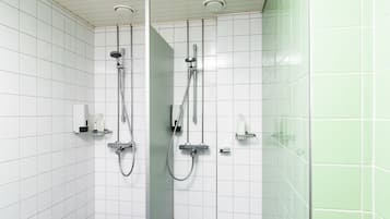 Un baño moderno con paredes de azulejos blancos, una cabina de ducha de cristal y un inodoro con dispensador de toallas de papel.