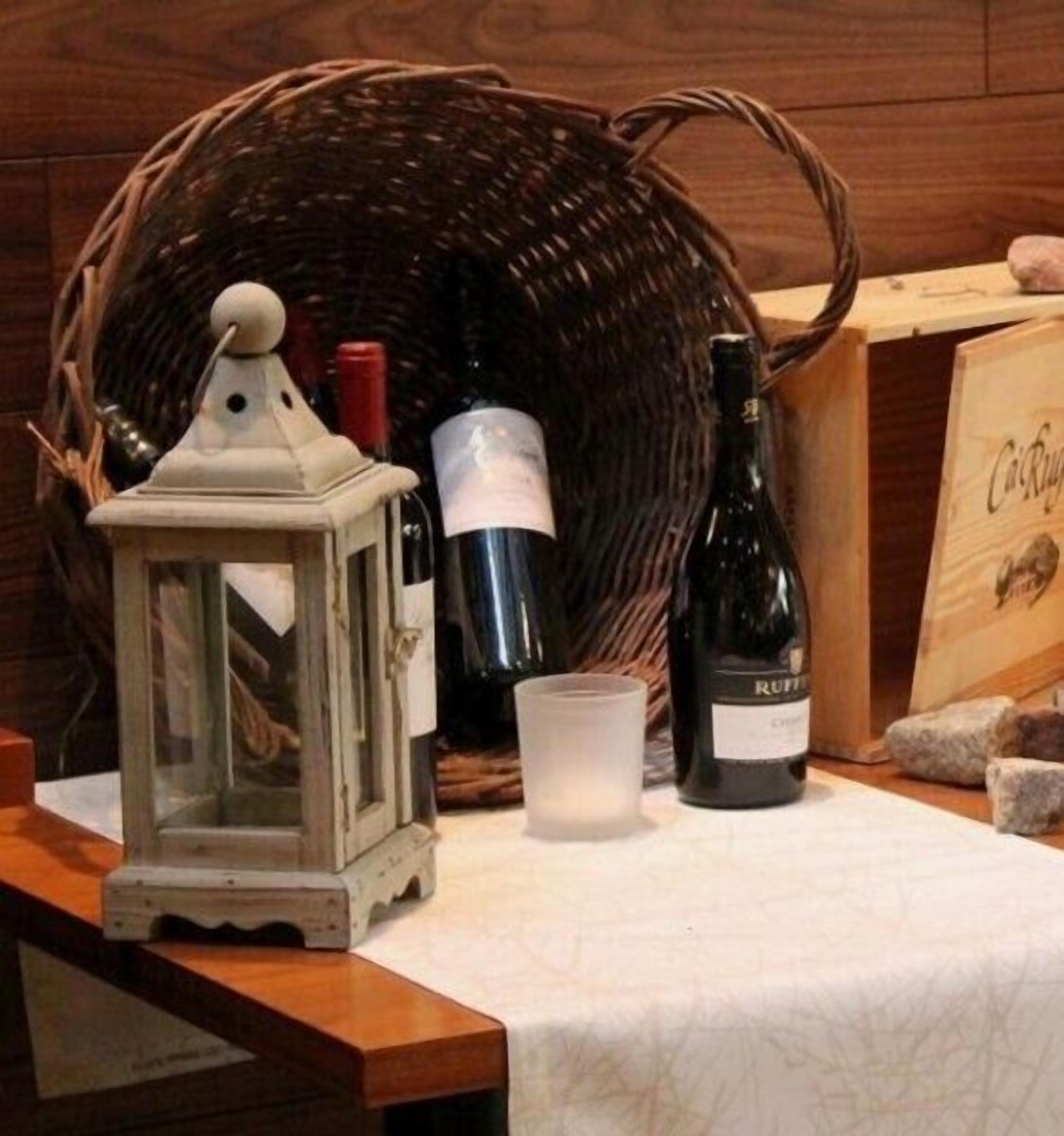 Una mesa con una cesta de mimbre, una vela, una botella de vino y un farol.