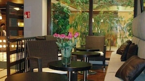 A cozy indoor seating area with wicker furniture, a coffee table with a vase of flowers, and a view of indoor plants through large windows. - Imatra Spa Sport Camp - Hostel (Imatra)