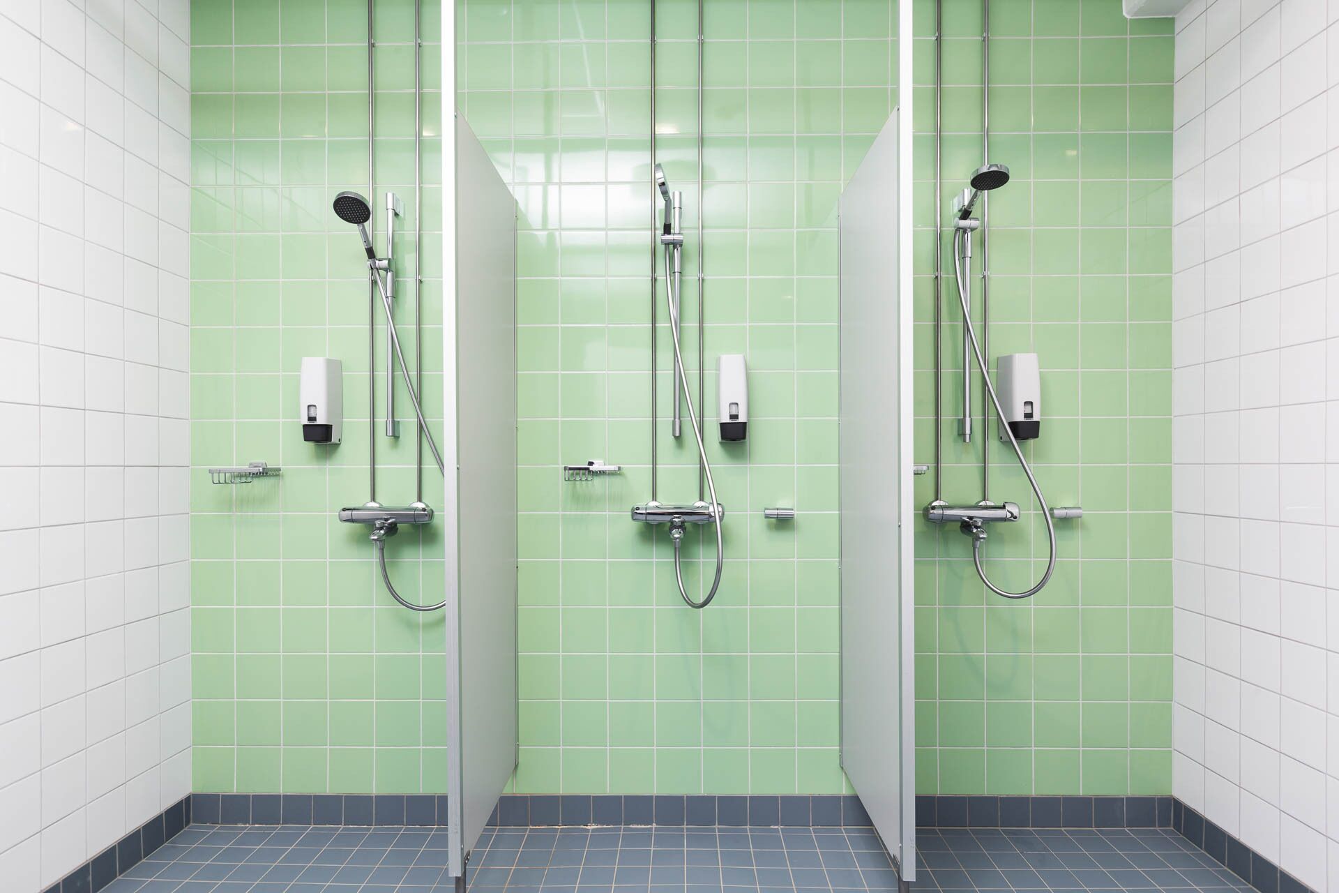 Une salle de bain avec des murs recouverts de carreaux verts, deux lavabos et un espace douche.