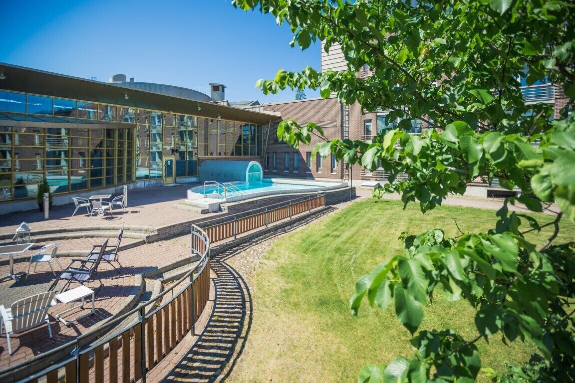 Un edificio moderno con piscina, mobiliario exterior y zona ajardinada.