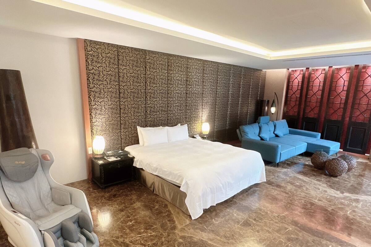 Quarto de hotel moderno com uma cama grande, uma cadeira de massagem, um sofá azul e uma parede estampada.