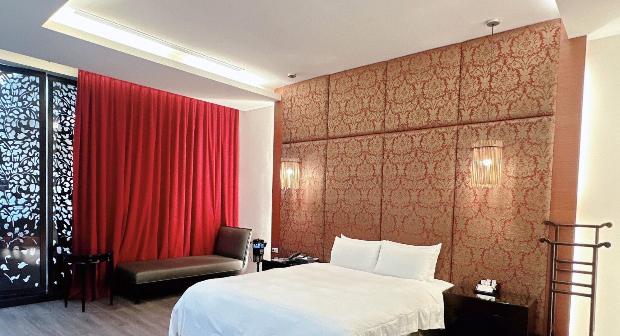 A hotel room with a bed, a desk, a chair, and a red curtain.