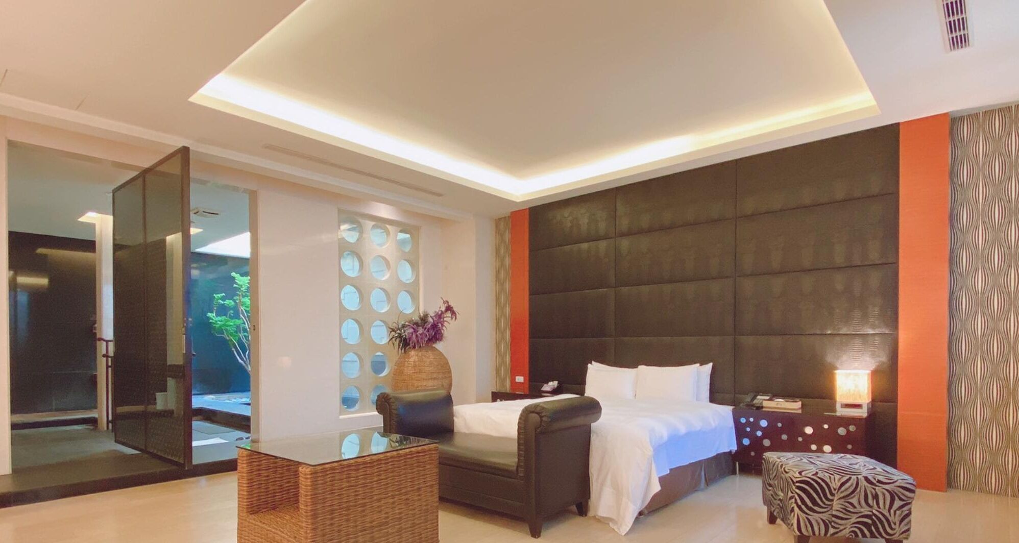 Una habitación de hotel moderna con una cama grande, una zona de estar, un separador de vidrio y un panel decorativo en la pared.