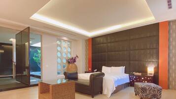 Una habitación de hotel moderna con una cama grande, una zona de estar, un separador de vidrio y un panel decorativo en la pared.