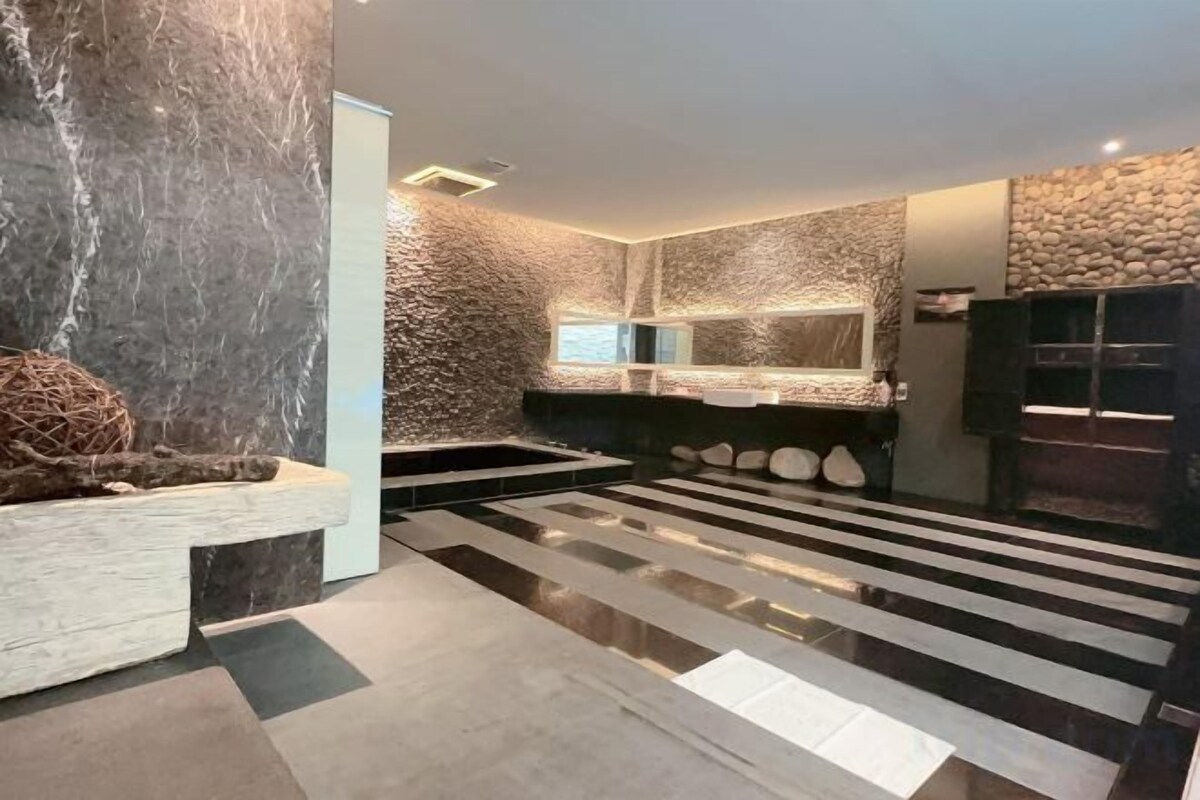 Un baño moderno con pared de mármol, un espejo grande y un banco de madera.