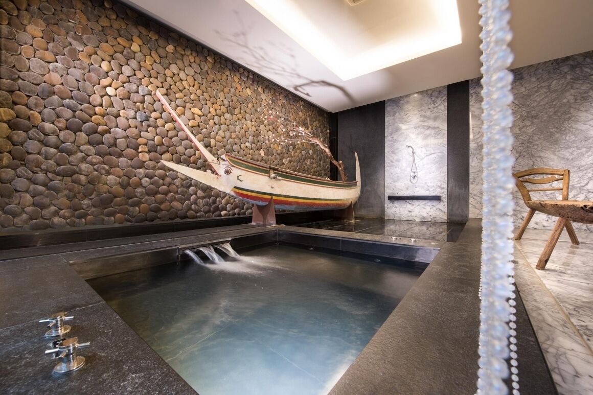Zona de spa con pared de piedra, un bote, una silla de madera y una fuente de agua.