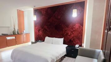 A modern hotel room with a large bed, a wooden dresser, a nightstand, and a red textured wall.
