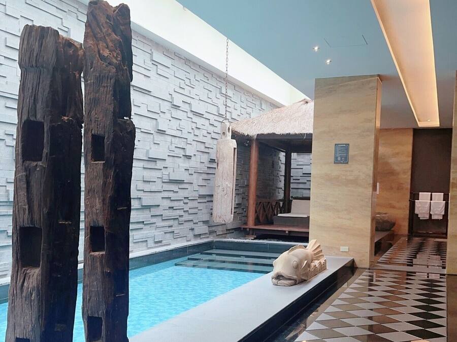 Un espace piscine intérieur moderne, agrémenté d’un mur en pierre, de sculptures en bois et d’un sol carrelé.