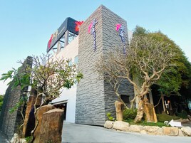 Un edificio moderno con fachada de piedra, señalización y árboles con jardines.