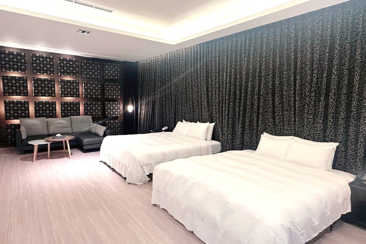 Quarto de hotel com duas camas, um sofá, uma mesinha e parede estampada.