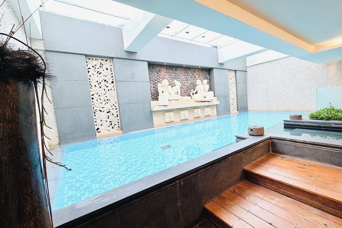 Piscina interior moderna com esculturas de pedra, um deck de madeira e um domo.